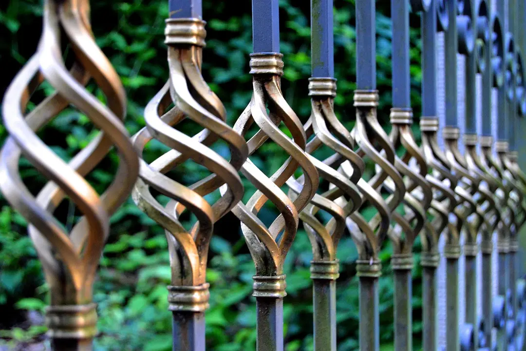 Close-up of twisting wrought-iron fence posts with greenery in the background