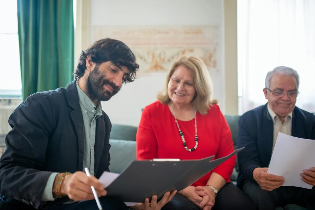 Three professionals sit together reviewing documents in a meeting about an HOA fidelity bond policy.