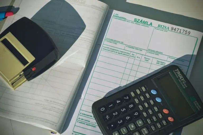 Close-up of a calculator and accounting papers on a desk, including an invoice form and writing tools.