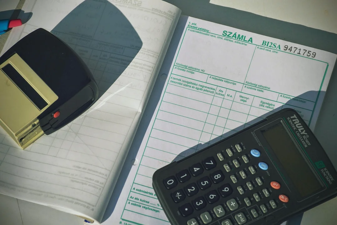 Close-up of a calculator and accounting papers on a desk, including an invoice form and writing tools.