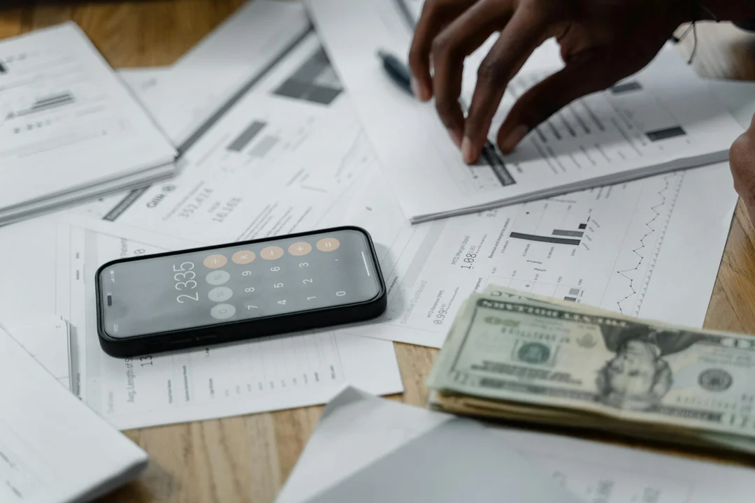 Close-up of financial documents, cash, and a smartphone on a desk with hands reviewing the materials.