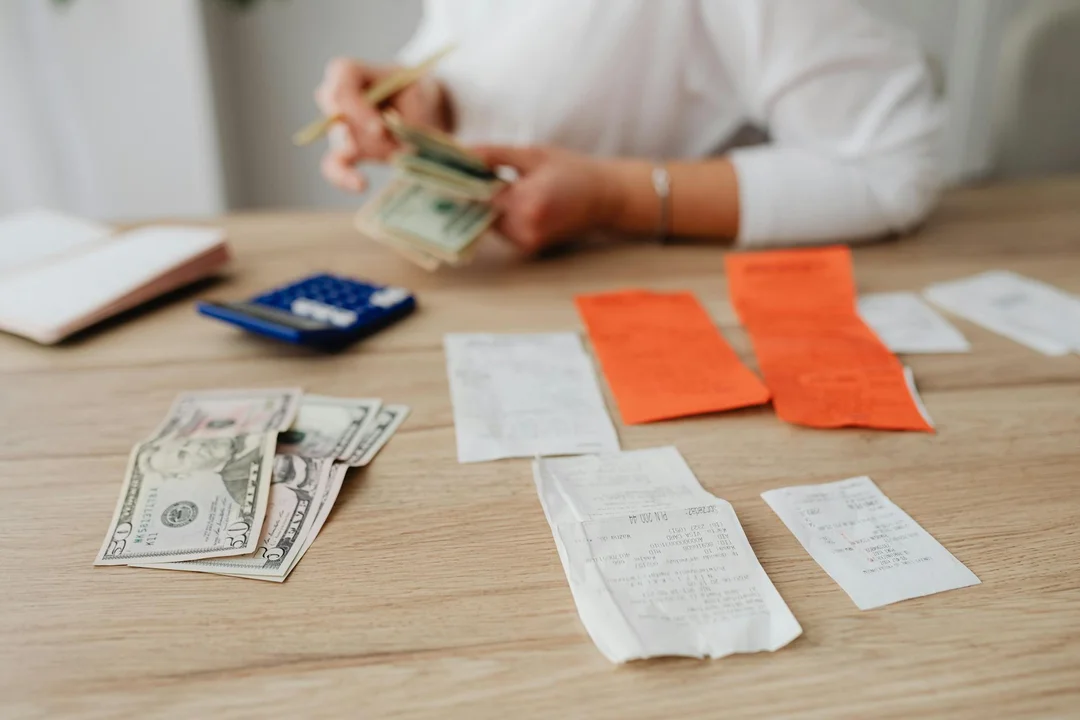 Close-up of hands counting cash with receipts and a calculator on a wooden table.
