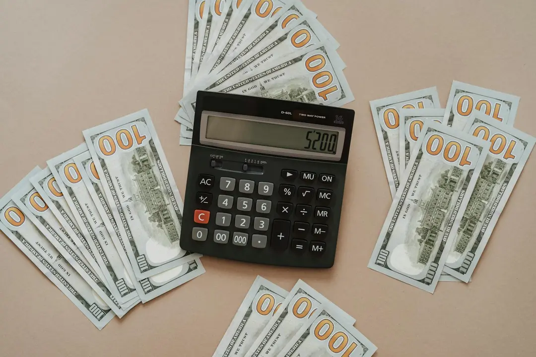 Calculator surrounded by scattered US 100-dollar bills, illustrating budgeting and financial analysis for HOA finances.