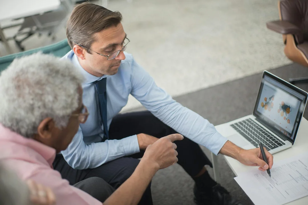 Two professionals review documents and a laptop displaying charts during an HOA financial planning meeting.