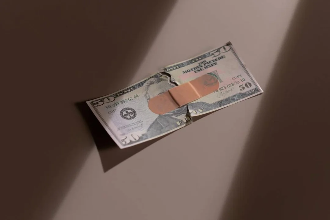 A torn fifty-dollar bill with a band-aid across the center on a neutral surface.