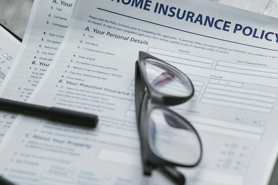 Glasses resting on a page of a home insurance policy form and other documents, representing reviewing compliance documents.