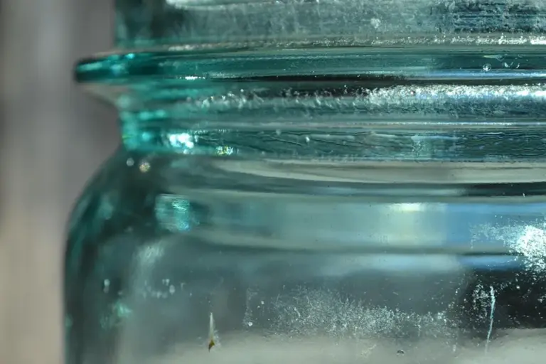 Close-up of a teal-tinted glass jar with a dusty interior.