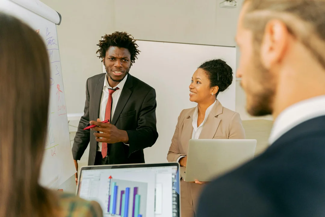 Diverse professionals in a conference room discuss data on a whiteboard and a laptop screen, illustrating collaborative planning for neighborhood value growth under HOA governance.