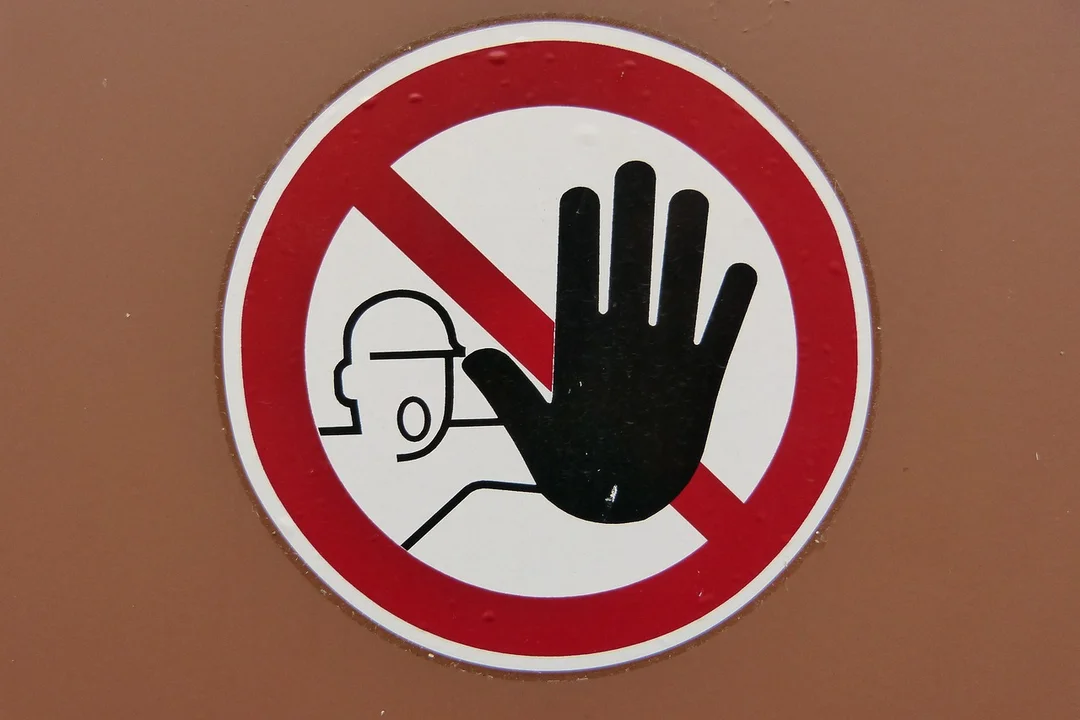 Circular sign with a red border showing a black raised hand in a stop gesture and a simple figure silhouette behind, indicating prohibition or stoppage.