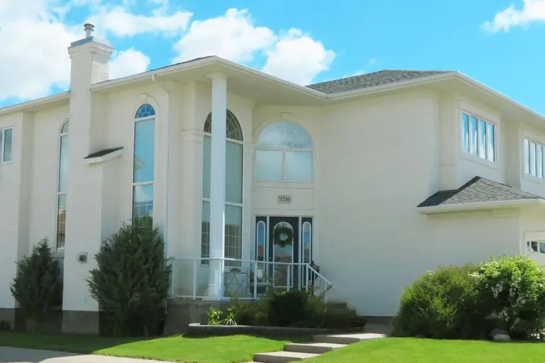 Front view of a white modern house with arched windows, a small front porch, and a manicured lawn.