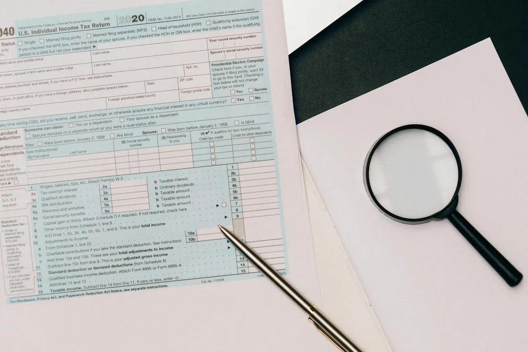 Close-up of tax forms on a desk with a magnifying glass and a pen, representing analysis of HOA income classifications for Form 1120-H.