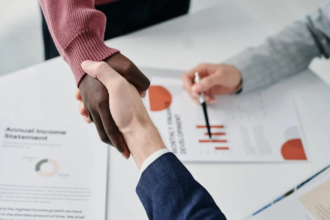 Handshake between two people over a table with documents and charts, symbolizing mediation in HOA disputes.