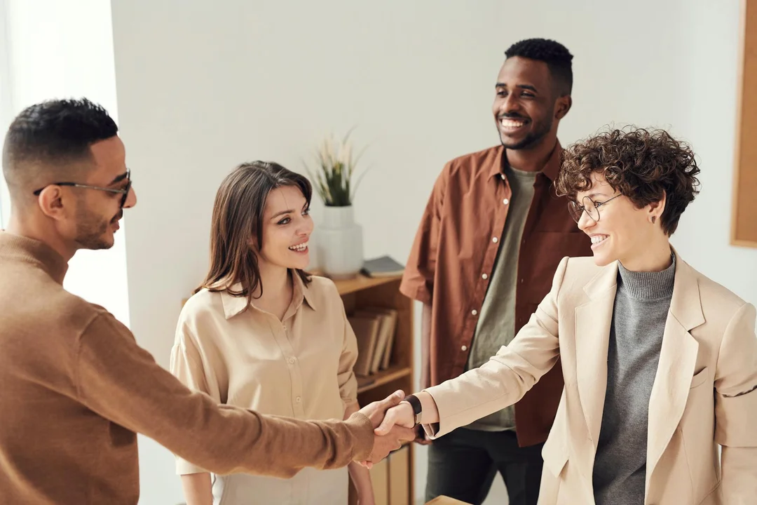 Diverse group of professionals in a bright office sharing a handshake and smiles, representing collaborative mediation.