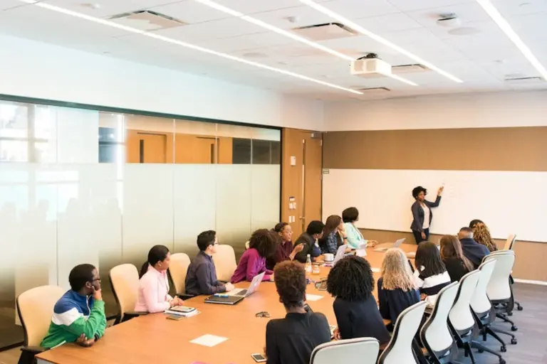 Diverse group of HOA members seated around a conference table while a presenter explains bylaws on a whiteboard in a bright meeting room.