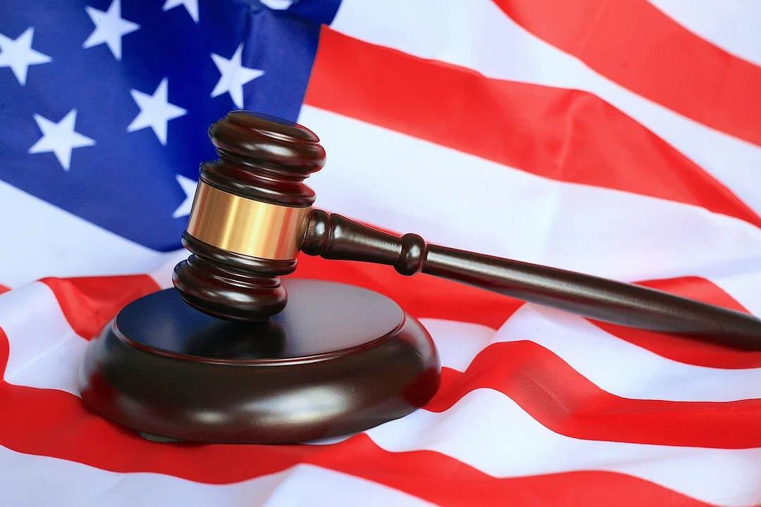 A wooden judge's gavel rests on a surface with an American flag in the background, symbolizing governance and rule-based decision making.
