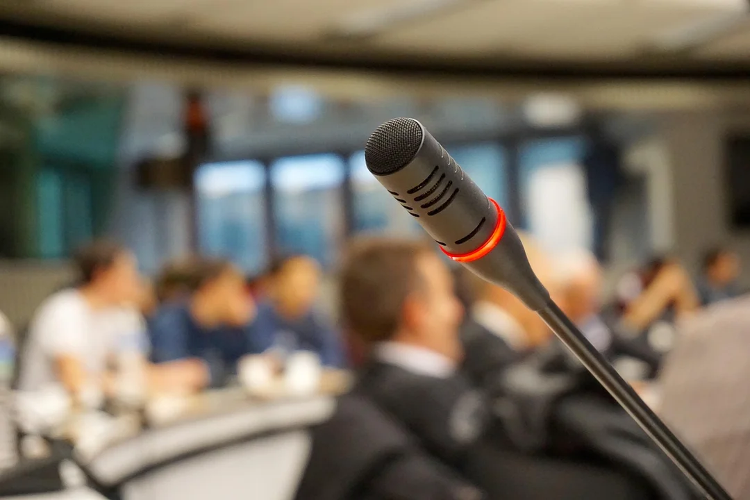 Close-up of a microphone at a conference table with attendees blurred in the background