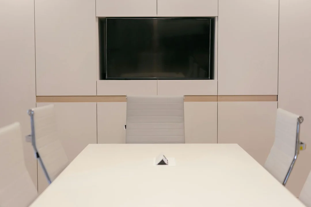 Modern HOA meeting room with a long white table, white chairs, and a large wall-mounted screen, prepared for a homeowners association meeting.
