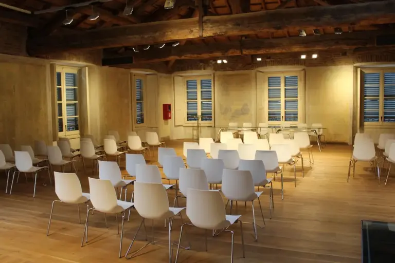 Empty conference room with exposed wooden beams, wooden floor, and rows of white chairs arranged for a meeting.