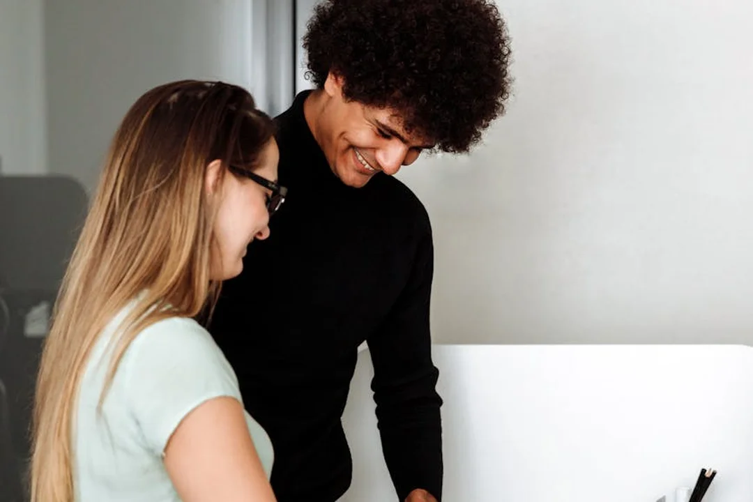 Two colleagues collaborating at a computer in an office, smiling as they review HOA meeting materials.