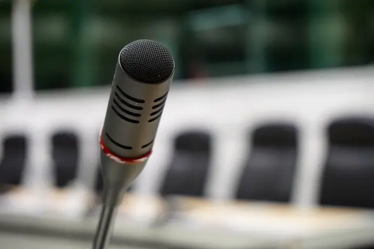 Close-up of a microphone at a meeting with blurry empty chairs in the background.