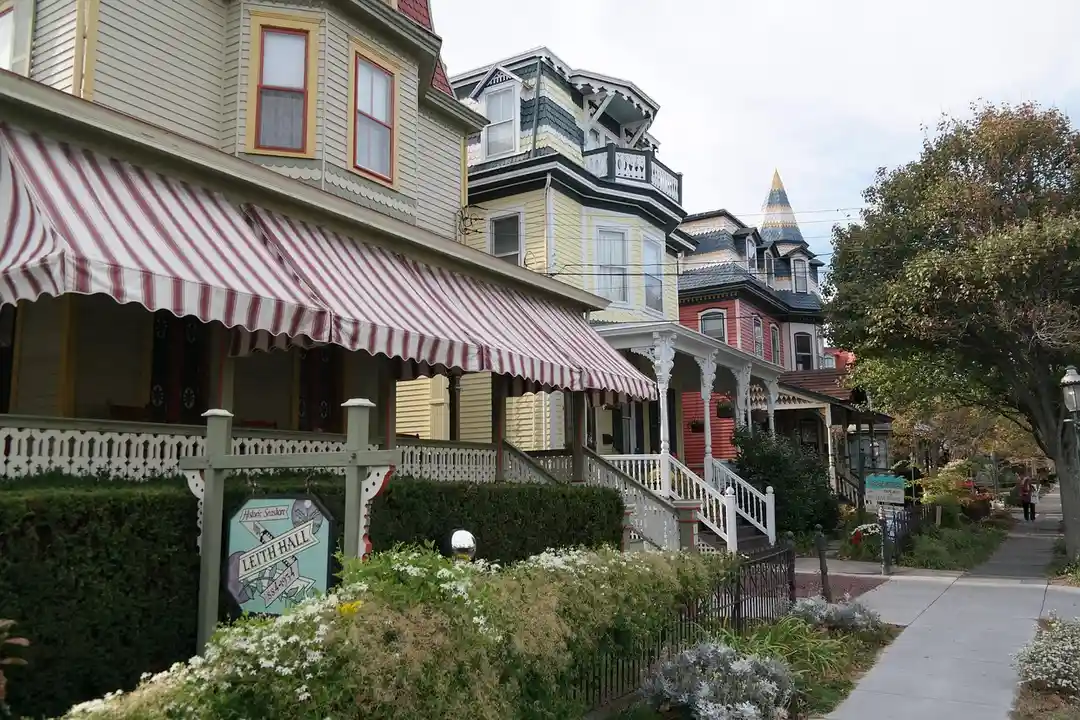 Row of colorful Victorian-style houses with striped awnings along a sidewalk in an HOA community.