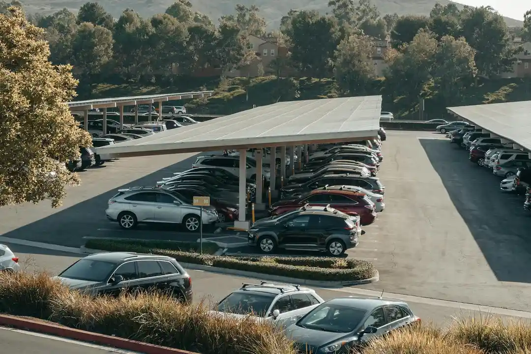 Aerial view of a HOA-managed parking lot with rows of cars parked under covered carports, surrounded by trees.