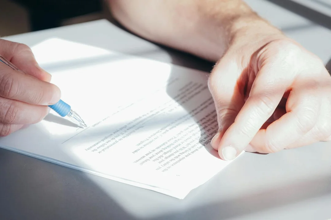Close-up of hands signing a document with a blue pen on a desk