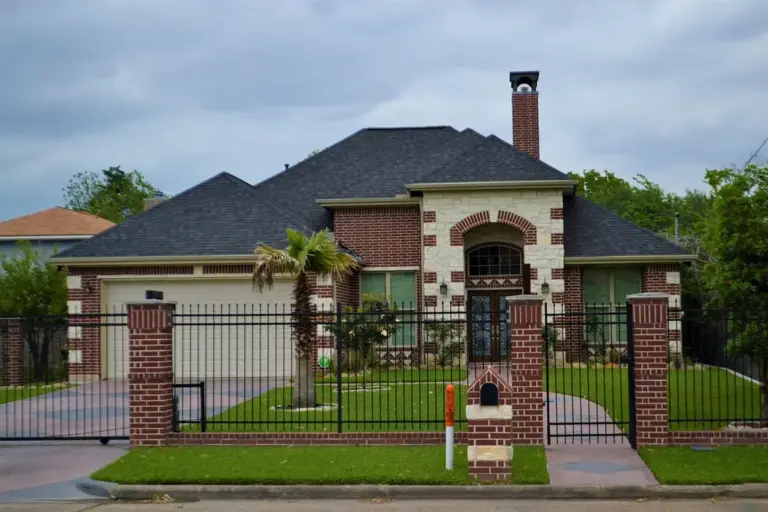 Front view of a suburban brick house with a gated iron fence in a homeowners association.