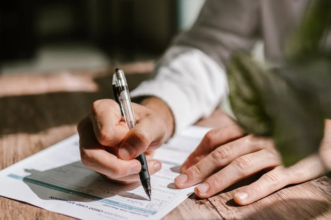 Close-up of hands writing on a form with a pen, preparing a report about HOA abuses.