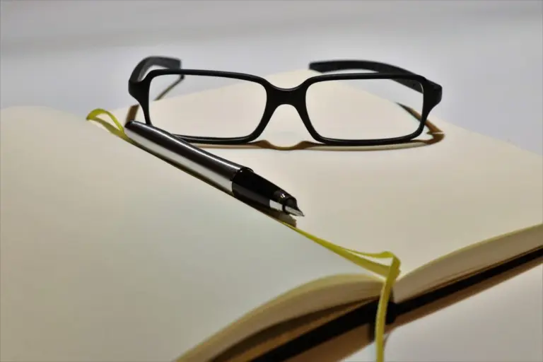 A pair of black-framed glasses resting on an open notebook with a pen nearby