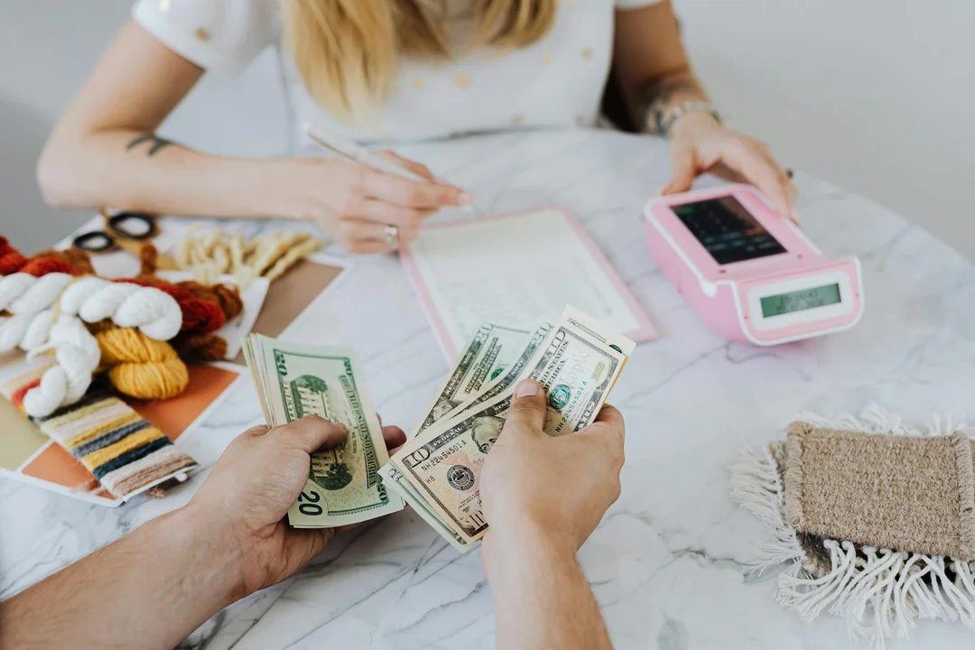 Two people at a table handling cash and documents, with a pink calculator, illustrating financial planning for HOA reserve funds.