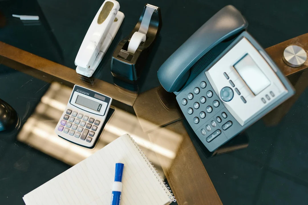 Office desk with a calculator, landline phone, notebook and pen, representing financial planning and communication for an HOA reserve fund.