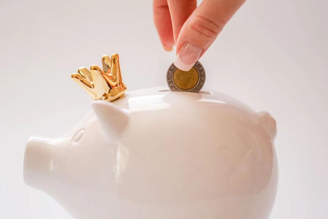 Hand placing a coin into a white piggy bank, illustrating saving for HOA reserve funds.