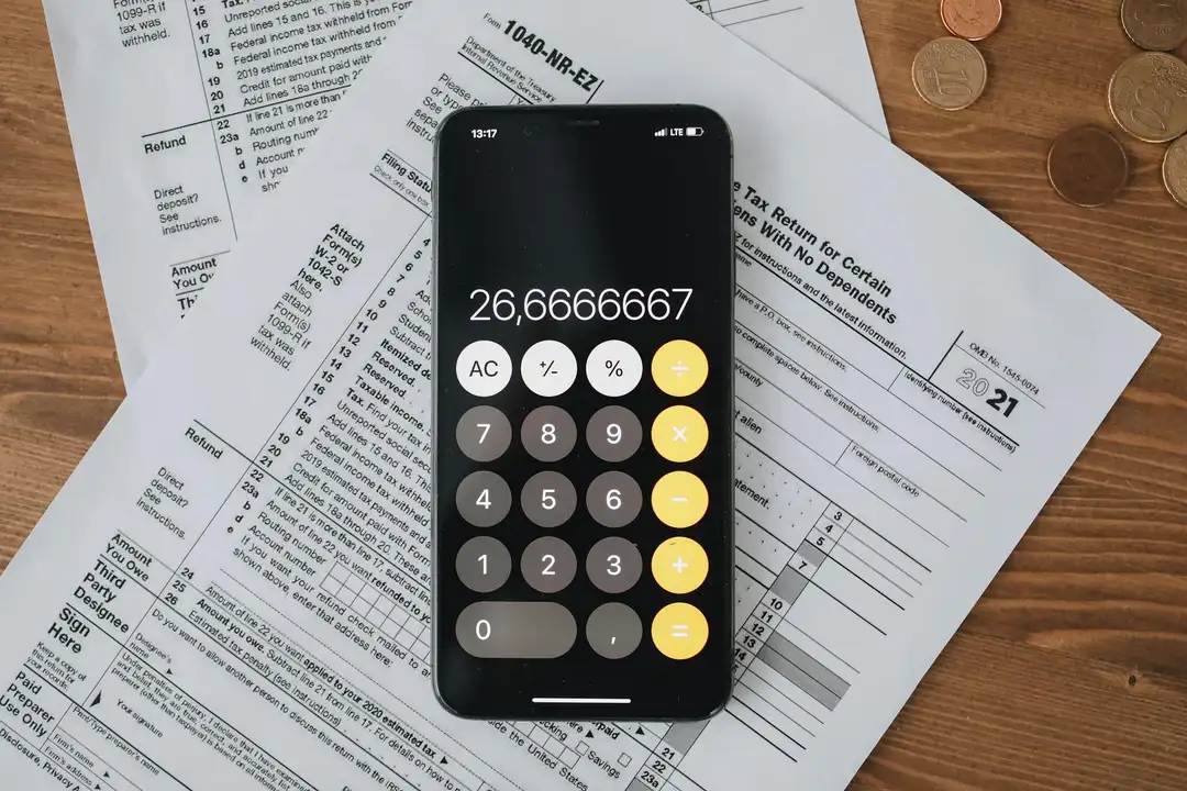 A smartphone displaying a calculator app rests on financial documents and coins spread across a wooden surface, illustrating HOA reserve fund planning.