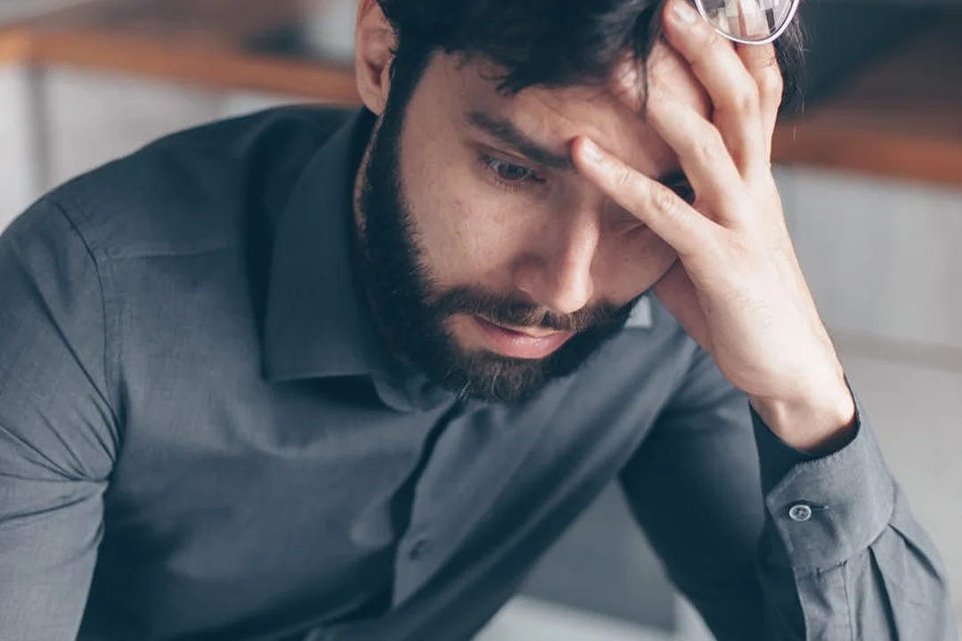 A worried man with a beard sits with his hand on his forehead, illustrating concern about HOA dues and notices.