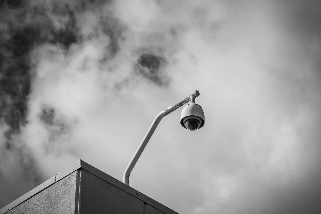 Surveillance camera mounted on the corner of a building against a cloudy sky.
