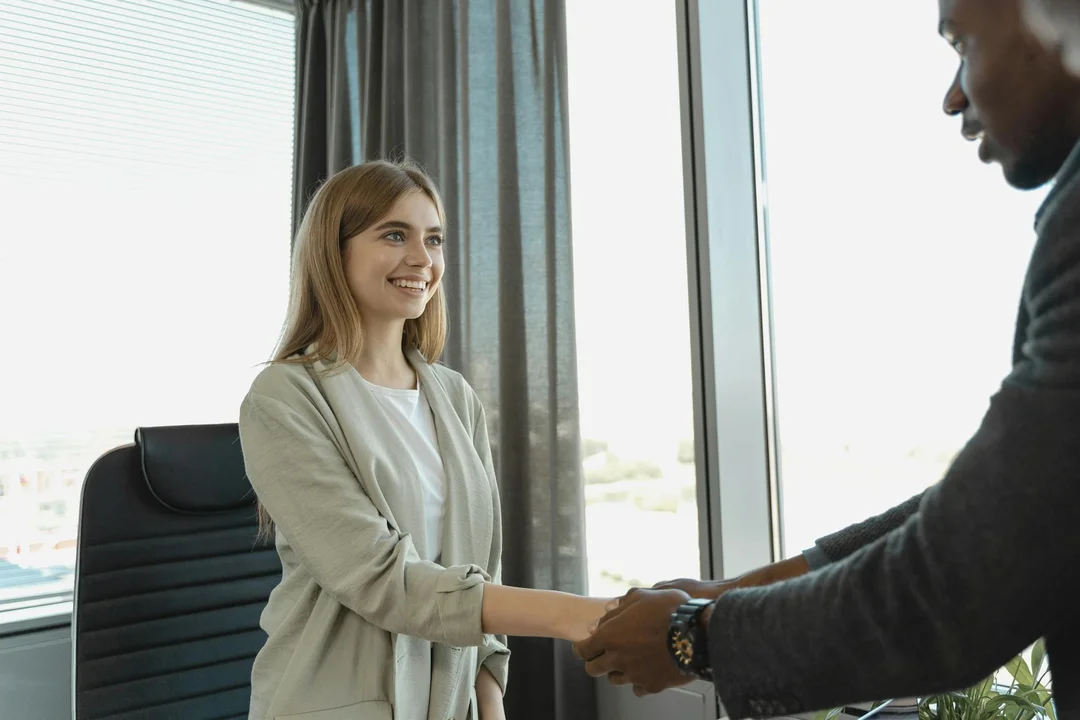 A woman and a man shake hands in an office, representing collaboration and a smooth leadership transition.