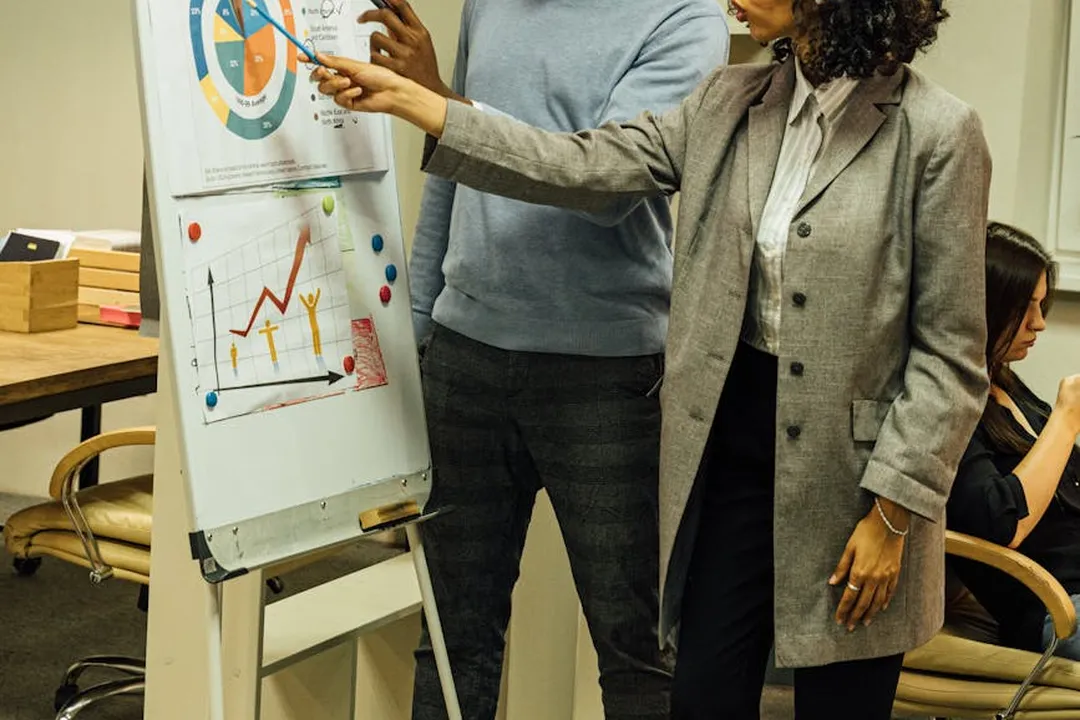 Two professionals standing by a whiteboard with charts and graphs, discussing HOA operational metrics and vendor performance.