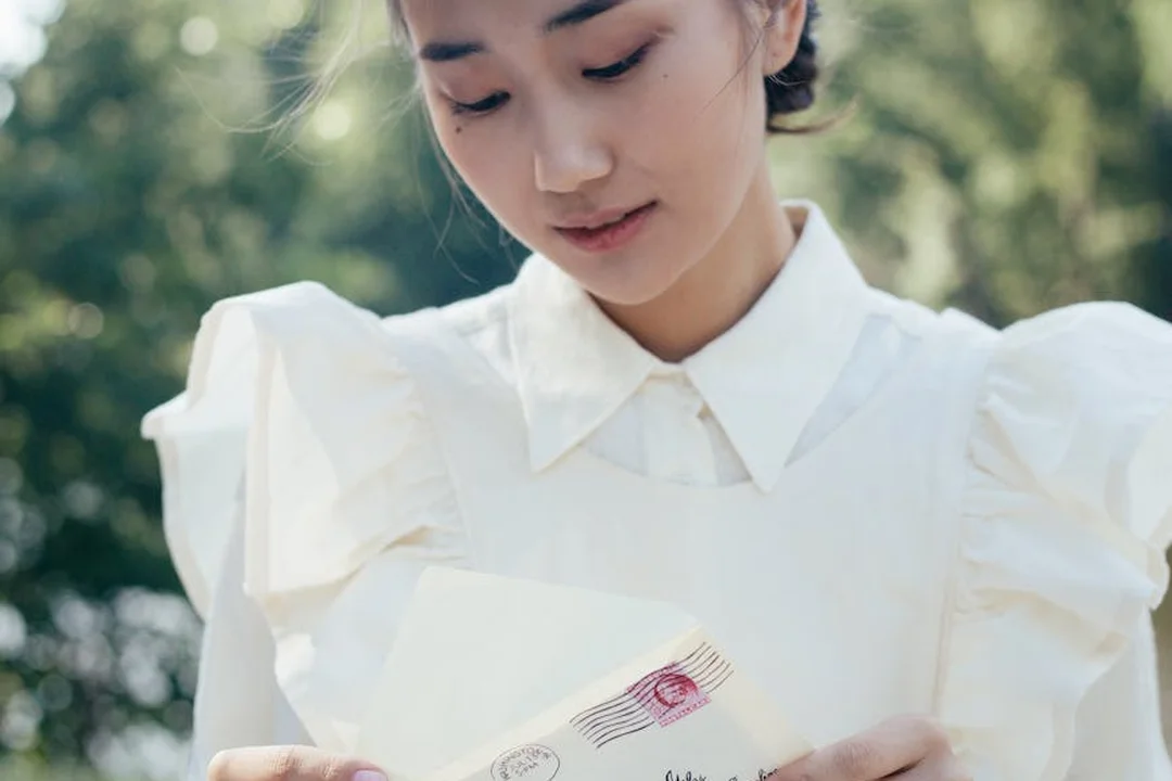 Person in a white blouse reading a letter outdoors