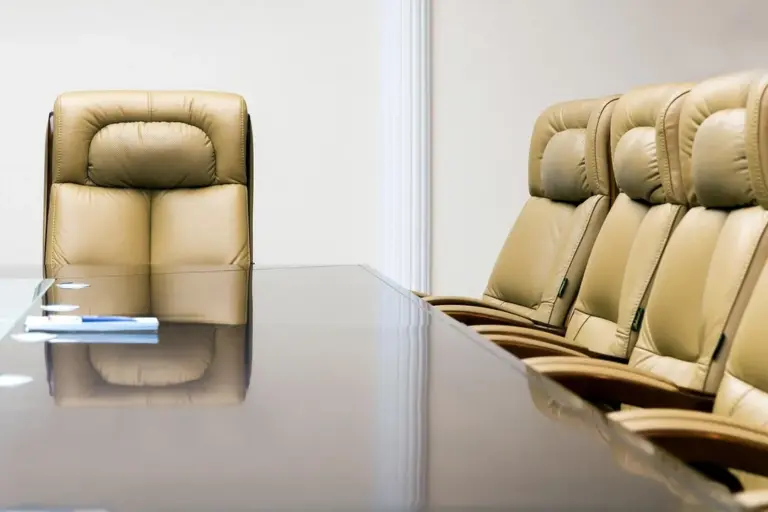 Empty boardroom with beige leather chairs around a glossy conference table.