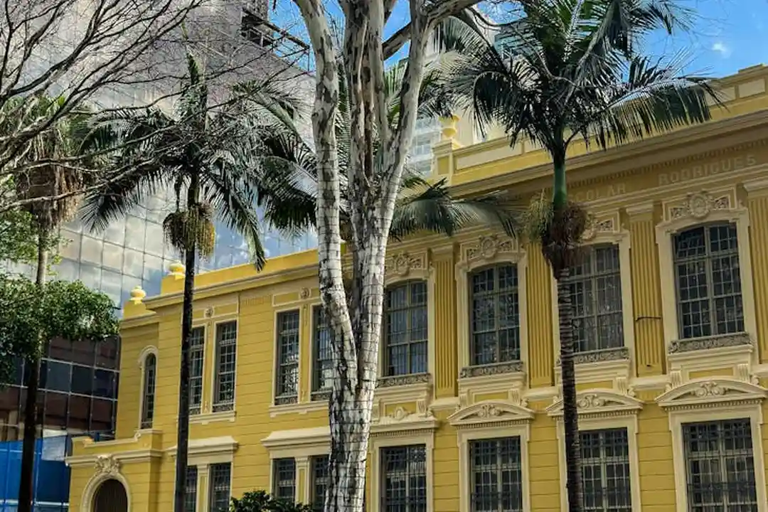 Yellow ornate building with tall arched windows and palm trees in front.