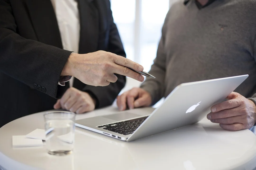 Two professionals sit at a round table examining a laptop, one holding a pen as they discuss fiduciary duties.