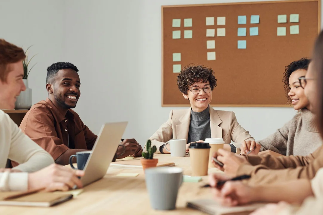 Diverse group of professionals seated around a conference table, collaborating on implementing and adapting an HOA's 5-year strategic plan, with a corkboard of sticky notes in the background.