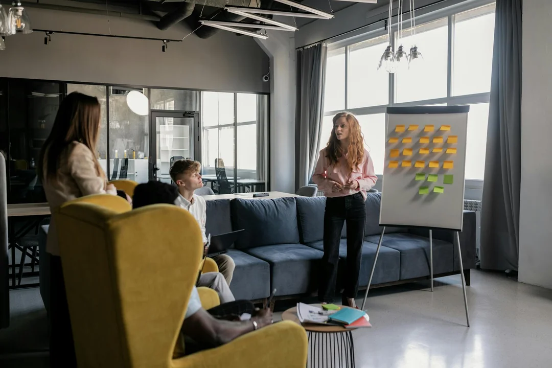 Three professionals in a modern office discuss decisions around a flip chart covered with colorful sticky notes.
