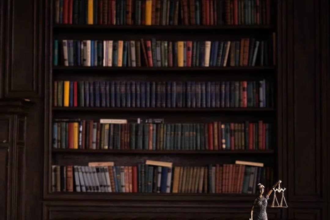 Dark wood bookshelf filled with colorful books and a small scales of justice statue in the lower right corner.