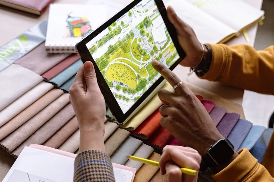 Hands holding a tablet displaying a landscape design while reviewing fabric swatches and planning notes.