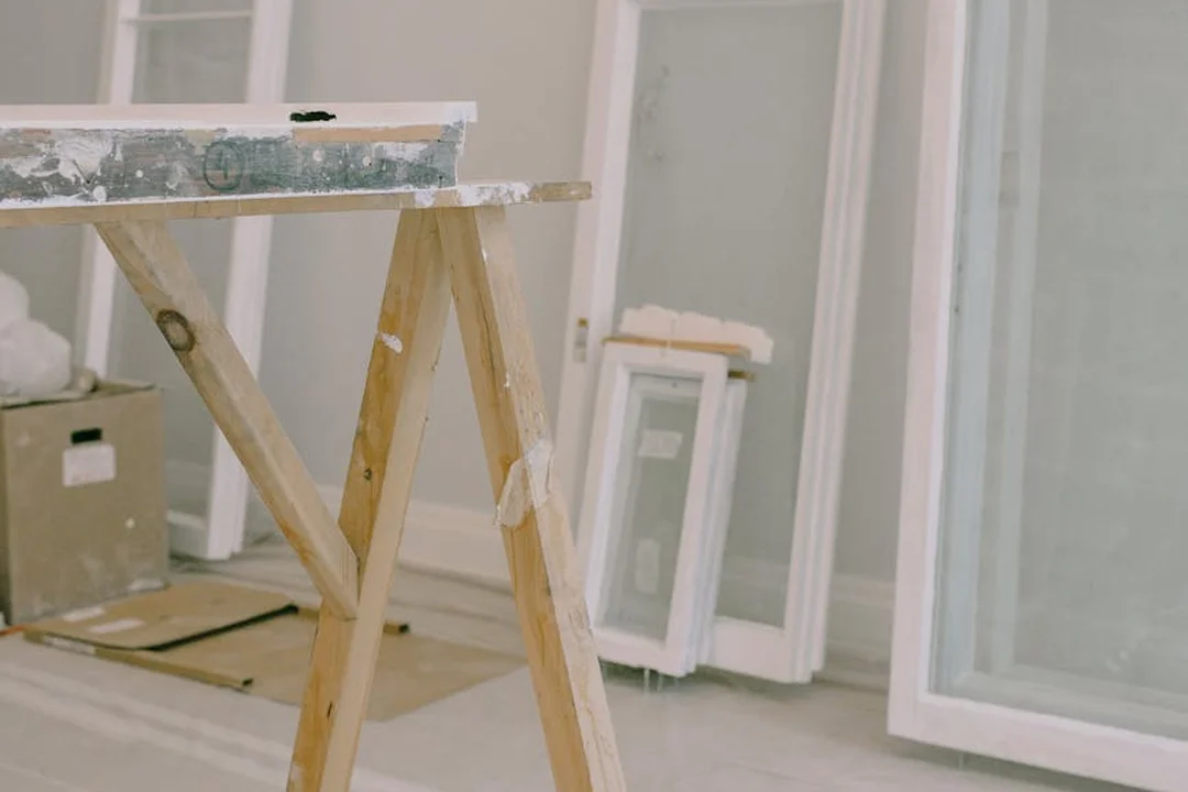 DIY renovation scene with a wooden sawhorse, a painted plank, and window frames in a home undergoing maintenance.
