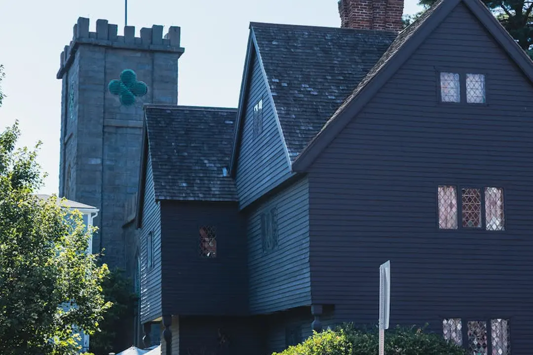 Dark blue two-story house with a tall stone tower in the background, featuring a green clover symbol on the tower.