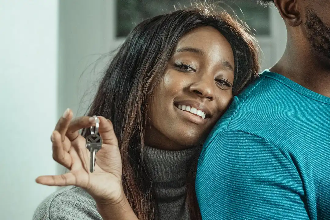 Smiling woman holds house key beside a man, representing a homebuyer considering HOA fees as part of the mortgage