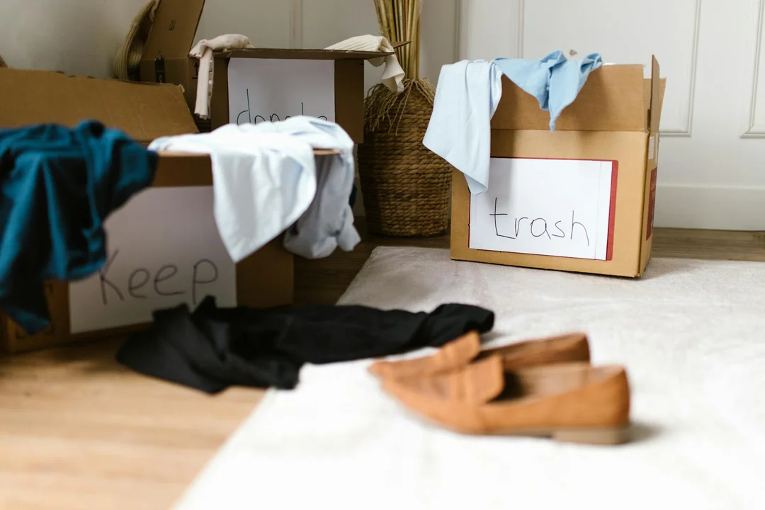 A room with moving boxes labeled 'keep' and 'trash', clothes and shoes scattered on the floor, symbolizing organizing and planning for proactive HOA compliance.